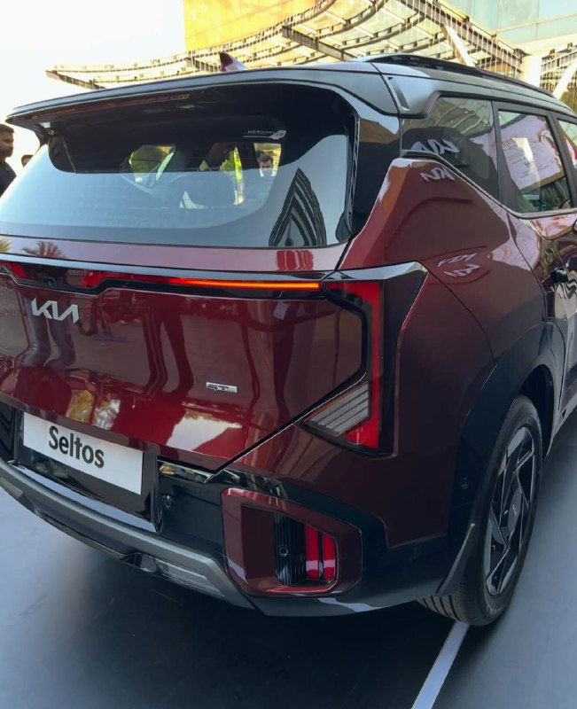 Крупный план задней части бордового KIA Seltos 2026 с декоративной светящейся линией и шильдиком модели на выставочной площадке.