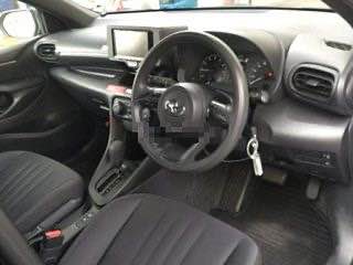 Салон Toyota Yaris 2021: фото передней части салона с рулём, панелью приборов, центральной консолью и передними креслами.