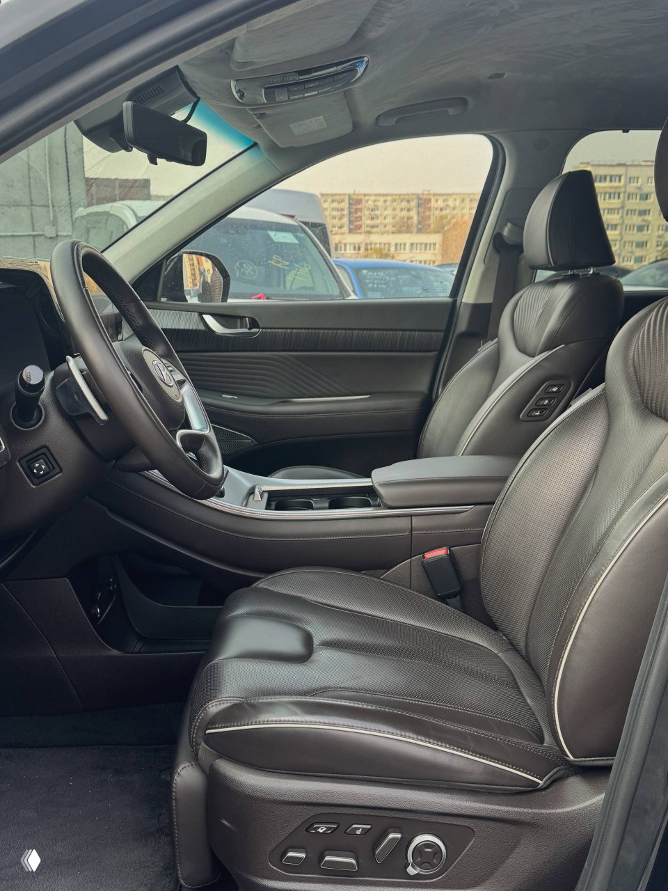 Передние сиденья и водительская зона: кожаная отделка кресел, подлокотник и элементы управления сиденьями, обзор салона с пассажирской стороны.