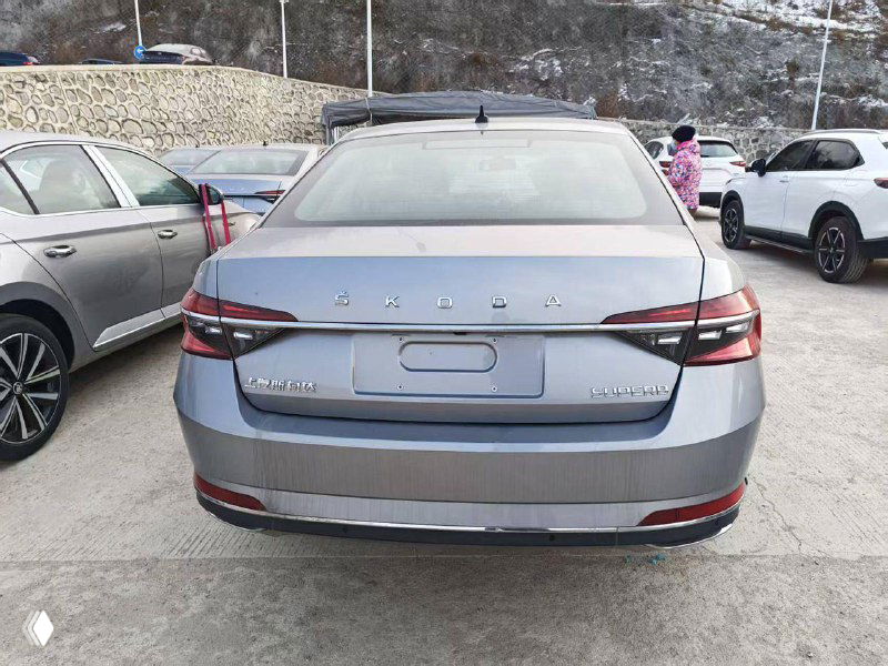 Задний ракурс серого Skoda Superb 2025 на площадке: вид багажника и шильд модели, автомобиль готов к транспортировке.