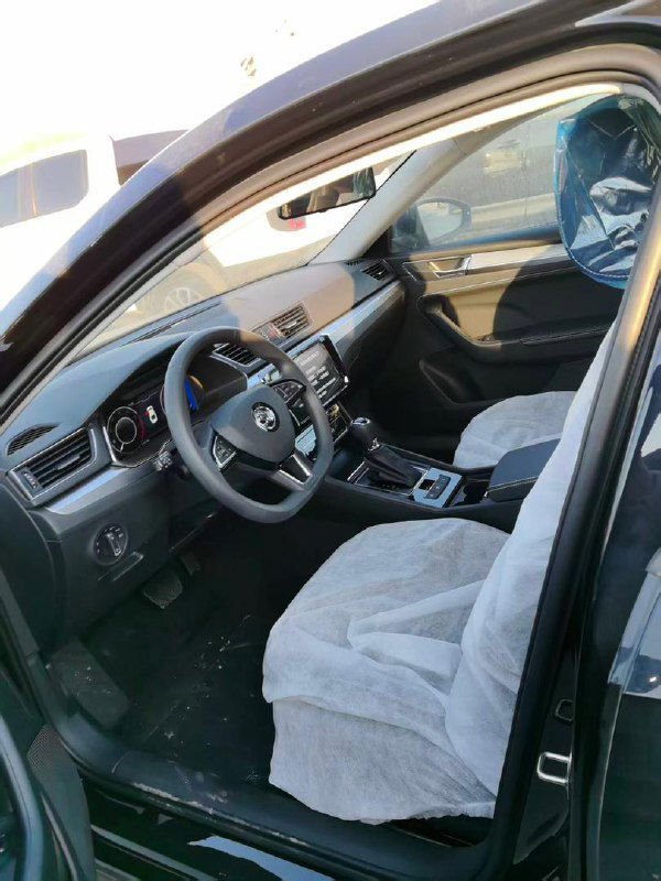 Интерьер Skoda Superb 2025: передние сиденья, руль и консоль, защитные чехлы на сиденьях при подготовке к отгрузке.