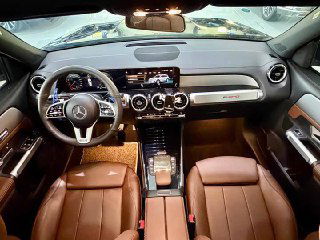 Салон Mercedes GLB 180 2022: панорамный вид приборной панели, мультимедиа экран, трехспицевый руль и коричневый кожаный салон с декоративной отделкой.