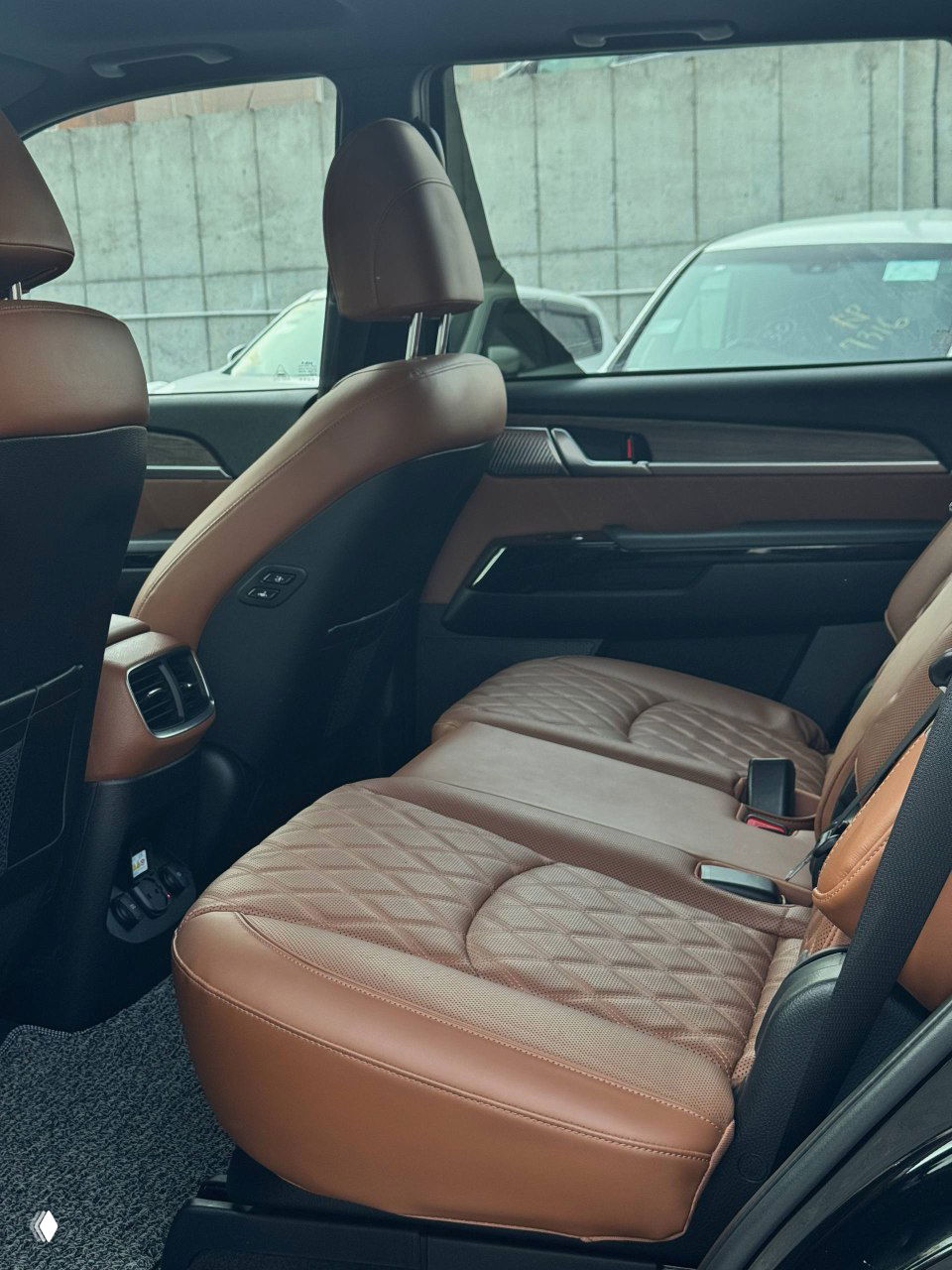 Вид на задний ряд сидений KIA Mohave — коричневые кожаные сиденья с прострочкой, достаточное пространство для пассажиров и вентиляционные дефлекторы.