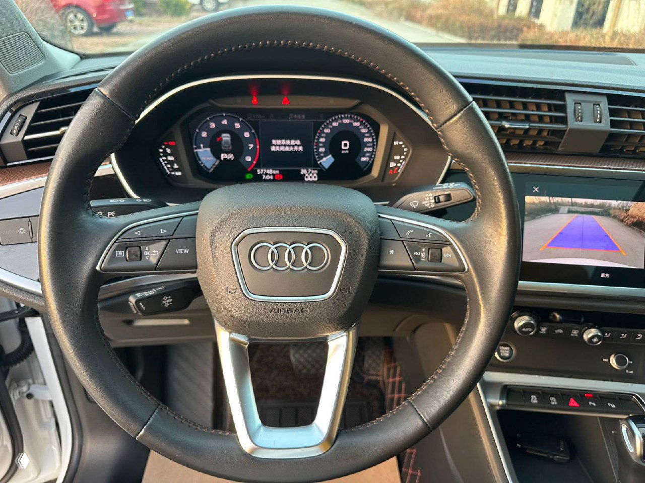 Крупный план рулевого колеса Audi Q3 с логотипом, приборная панель и индикаторы видны за ним; фотография демонстрирует состояние обшивки и органов управления.