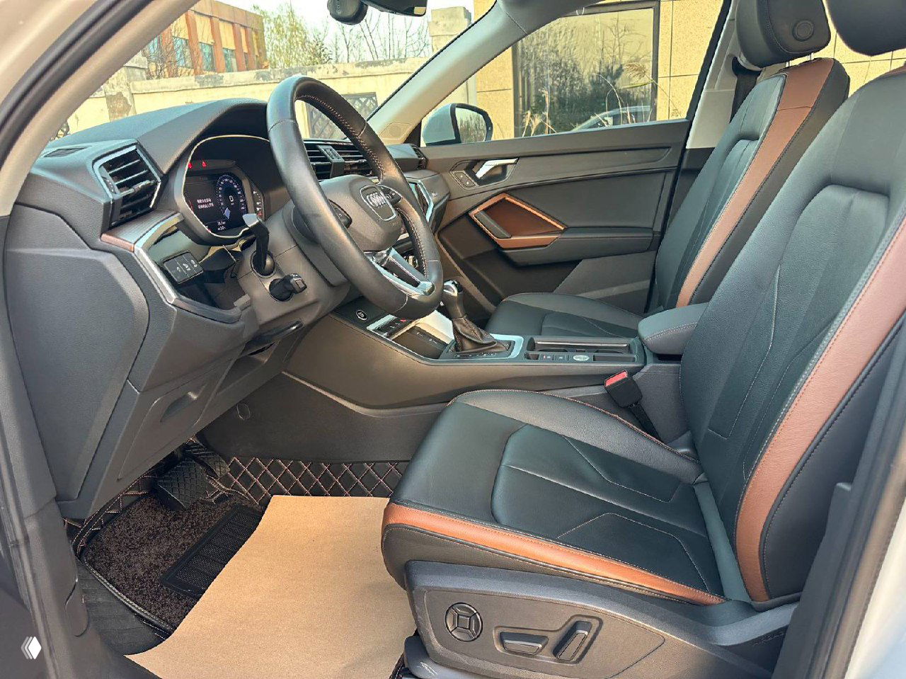 Крупный план центрального туннеля: селектор передач, панель кнопок и подстаканники Audi Q3; демонстрирует состояние отделки и эргономику центральной консоли.