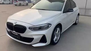 Видео-стил кадр белого BMW 1‑Series (120i) 2021, общий внешний вид спереди-сбоку, подчёркнута форма бампера и спортивная оптика комплектации M‑Sport.