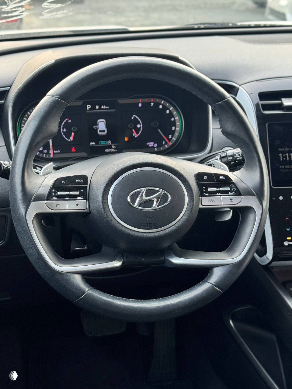 Крупный план рулевого колеса Hyundai с логотипом, вид на цифровую панель приборов и элементы управления мультимедиа в салоне автомобиля.