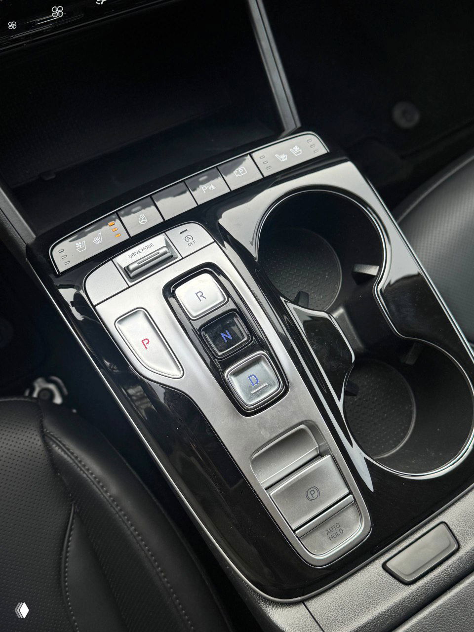 Блок управления режимами движения и кнопки селектора Hyundai Tucson рядом с подстаканниками, вид крупным планом на глянцевую панель.