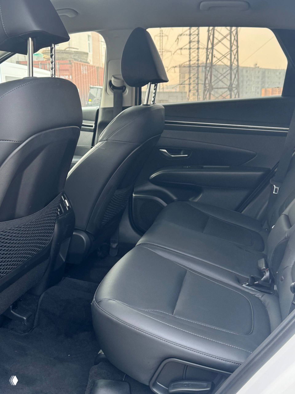 Задний ряд сидений Hyundai Tucson: кожаные сиденья, свободное пространство для ног и вид на дверные панели и окна грузовой стоянки.