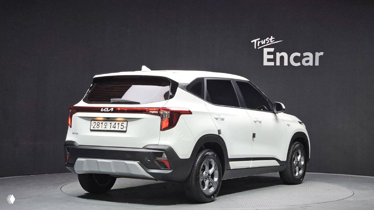 KIA Seltos 2023 белого цвета, вид сзади и в профиль в шоуруме Encar; видна задняя светотехника, бампер и номер Южной Кореи на авто.