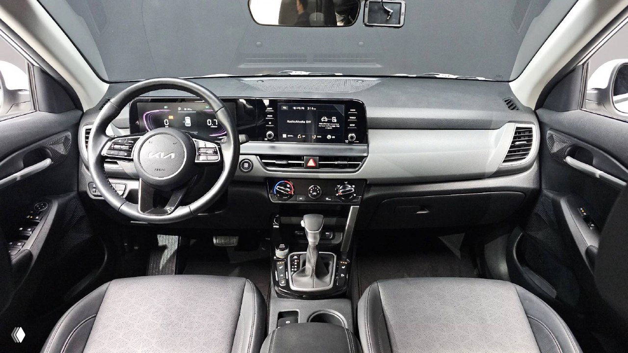 Салон KIA Seltos 2023: общий вид панели приборов, руль с логотипом KIA, центральная консоль и два передних кресла с отделкой.
