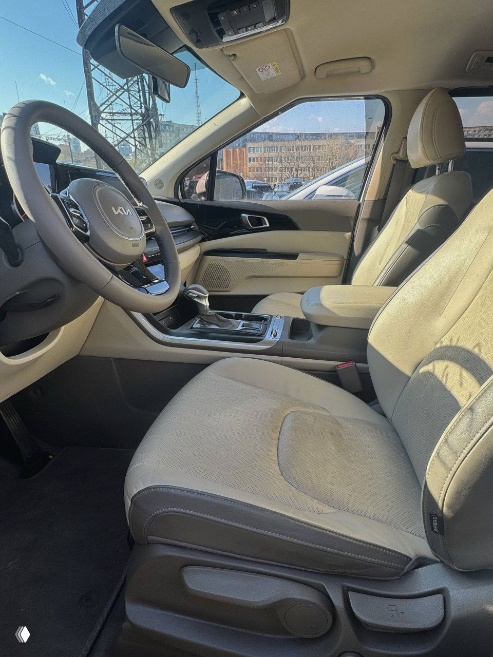 Вид на передние сиденья и панель со стороны пассажира: светлая обивка салона, центральный подлокотник и обзор через боковое окно.