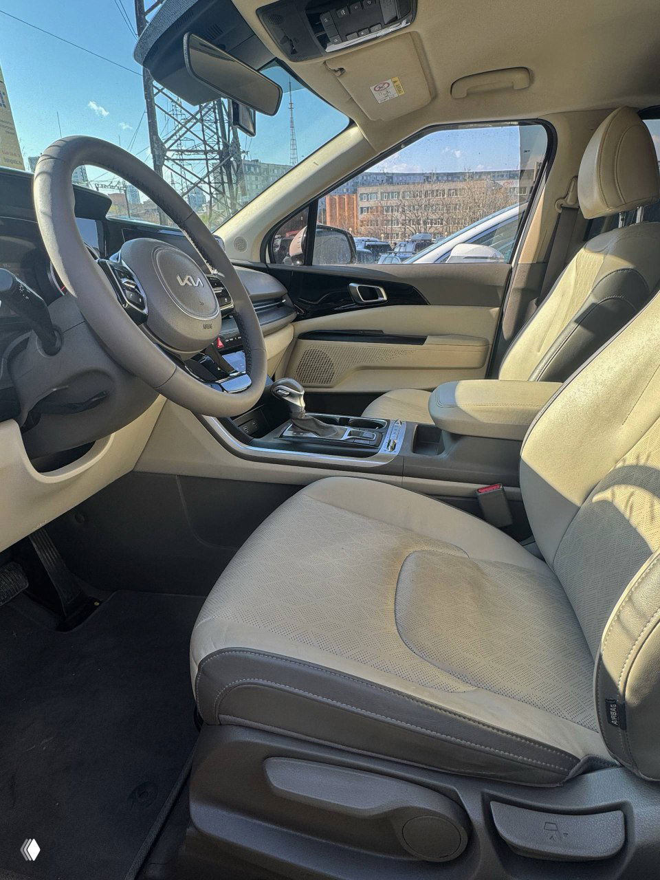 Передние сиденья KIA Carnival крупным планом: светлая тканевая обивка, регулировки положения и чистый салон с хорошим состоянием.