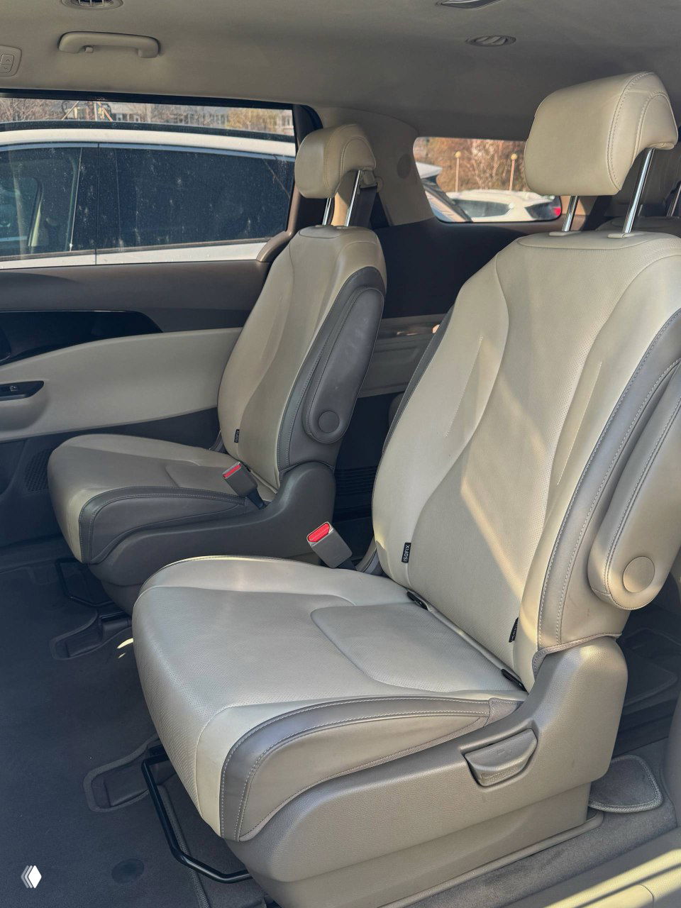 Средние сиденья минивэна KIA Carnival: два отдельных кресла второго ряда, видно направляющие и место для ног, интерьер в дневном свете.