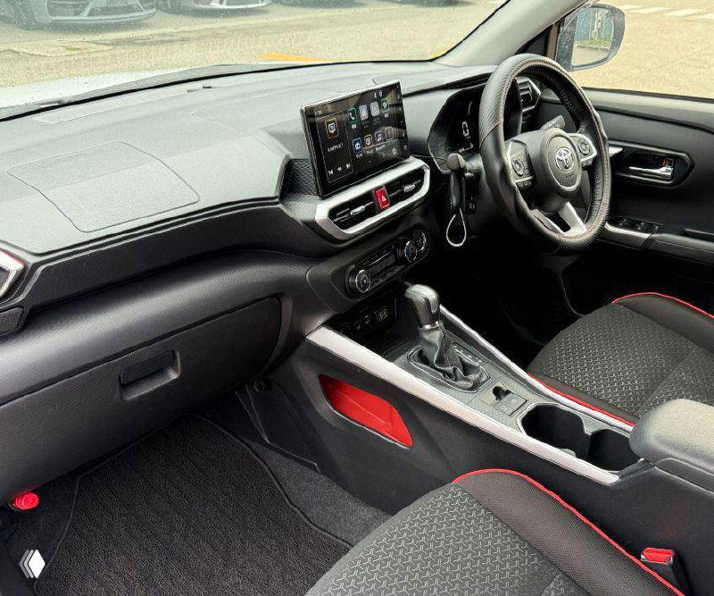 Интерьер Toyota Raize: центральная консоль с сенсорным дисплеем, рычаг переключения передач и тканевые сиденья с декоративными вставками.