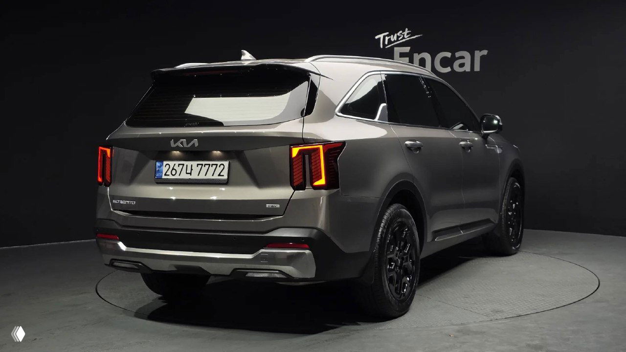 Задняя полубоковая проекция KIA Sorento 2024 с открытой пластиковой панелью багажника и включёнными задними фонарями на вращающейся платформе.