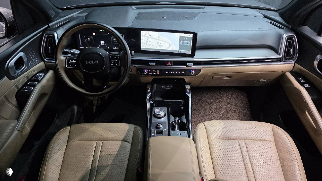 Фотография салона KIA Sorento: панорамный вид на приборную панель, центральный дисплей и бежевую отделку передних сидений, аккуратный торпедо.