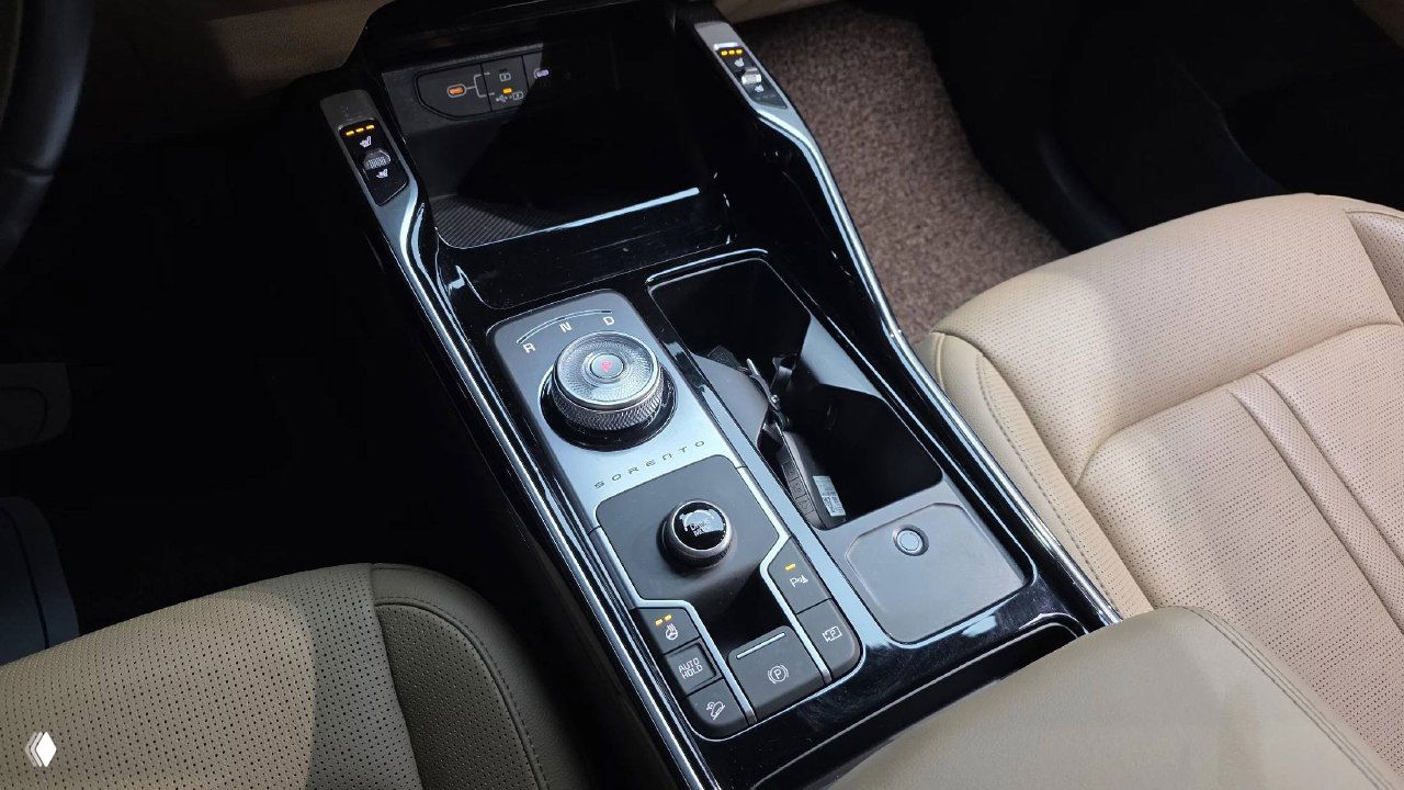 Крупный план центрального туннеля KIA Sorento 2024 — селектор режимов движения, элементы управления и подстаканники на глянцевой чёрной панели.