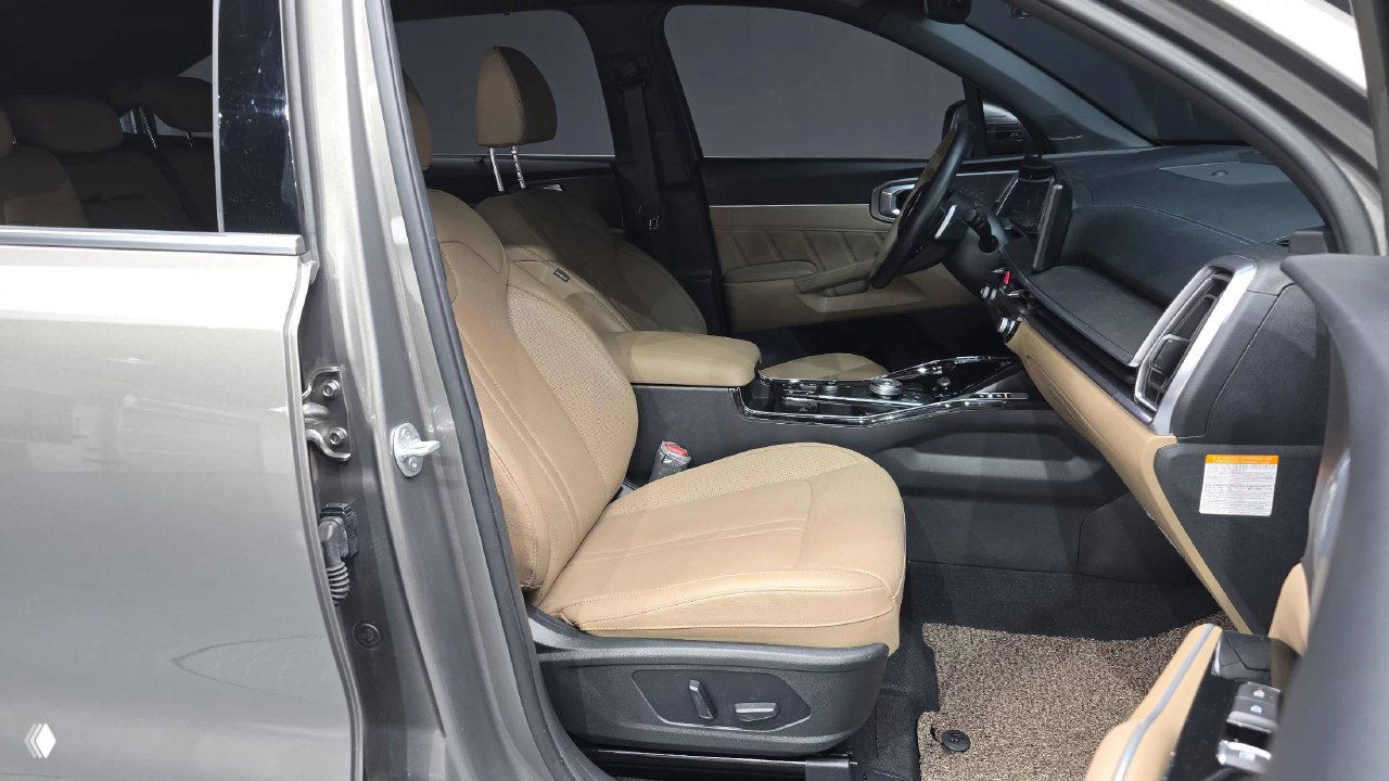 Фото салона со стороны пассажирской двери — бежевые передние сиденья, центральный подлокотник и просторный вход в салон KIA Sorento 2024.