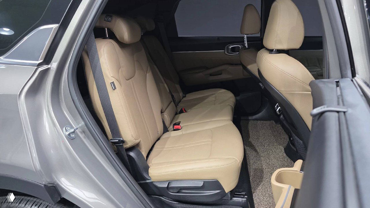 Вид задних сидений KIA Sorento 2024: бежевые кожаные сиденья, ремни безопасности и хорошо читаемый интерьер задней части кабины.