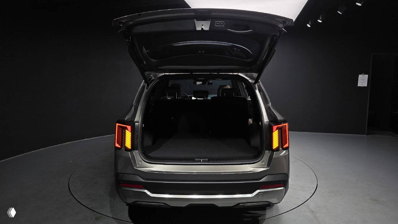 Открытый багажник KIA Sorento 2024: вид сзади в шоуруме, глубокое грузовое пространство и поднятая крышка багажника на вращающейся платформе.