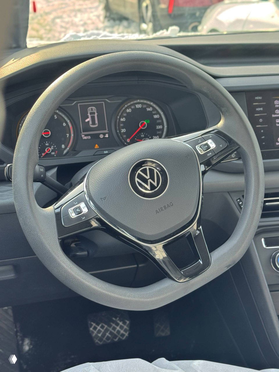 Крупный план рулевого колеса Volkswagen Tharu с эмблемой VW, вид торпедо и приборной панели; видно кнопки на руле и показания приборов.