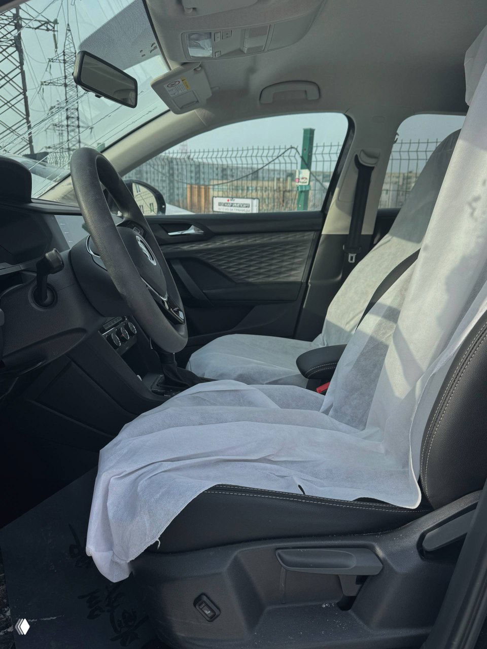 Передние сиденья Volkswagen Tharu защищены одноразовыми чехлами, вид сбоку на салон, руль и пространство для ног в салоне автомобиля.