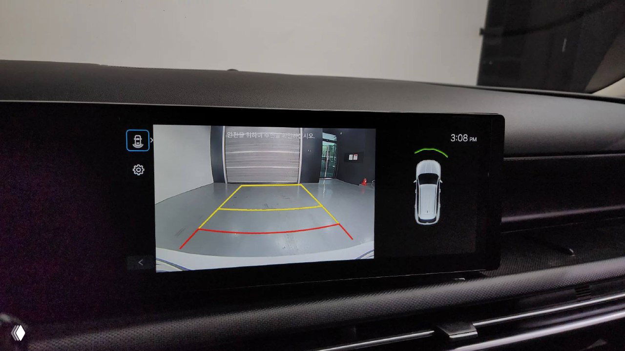 Экран мультимедиа показывает изображение с камеры заднего вида и схему парктроников, видна часть приборной панели и навигации автомобиля.