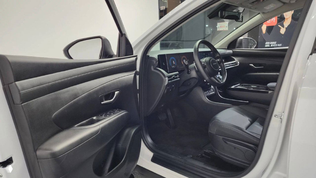 Открытая дверца водителя и вид на переднюю пассажирскую зону: чёрная обивка дверей, сиденья и элементы управления стеклоподъёмниками Hyundai Tucson.