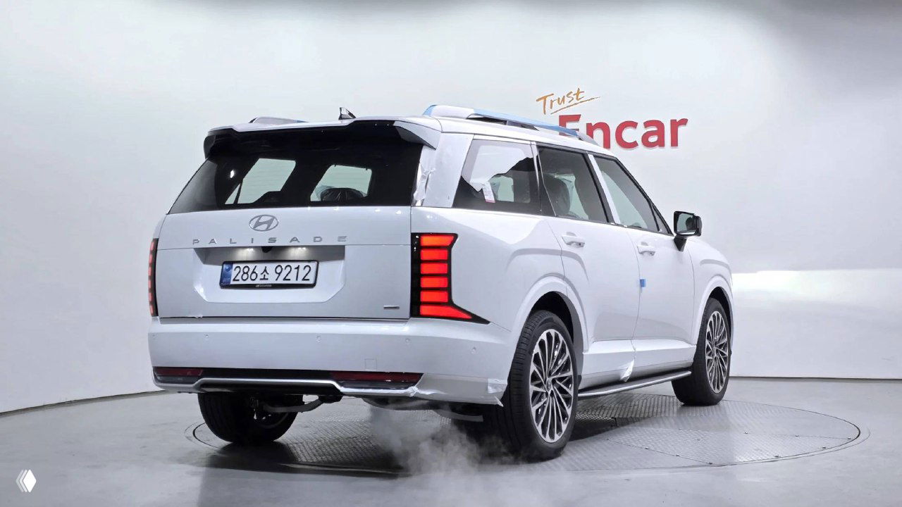 Задний ракурс белого Hyundai Palisade 2026 в салоне, видна открытая багажная дверь, вертикальные светодиодные фонари и южнокорейский номер.