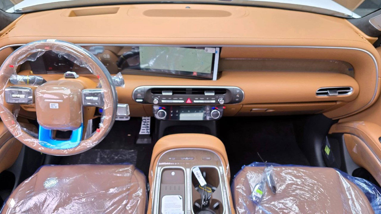 Интерьер Hyundai Palisade с коричневой кожаной отделкой, рулём и центральной консолью, передние сиденья в защитной плёнке.