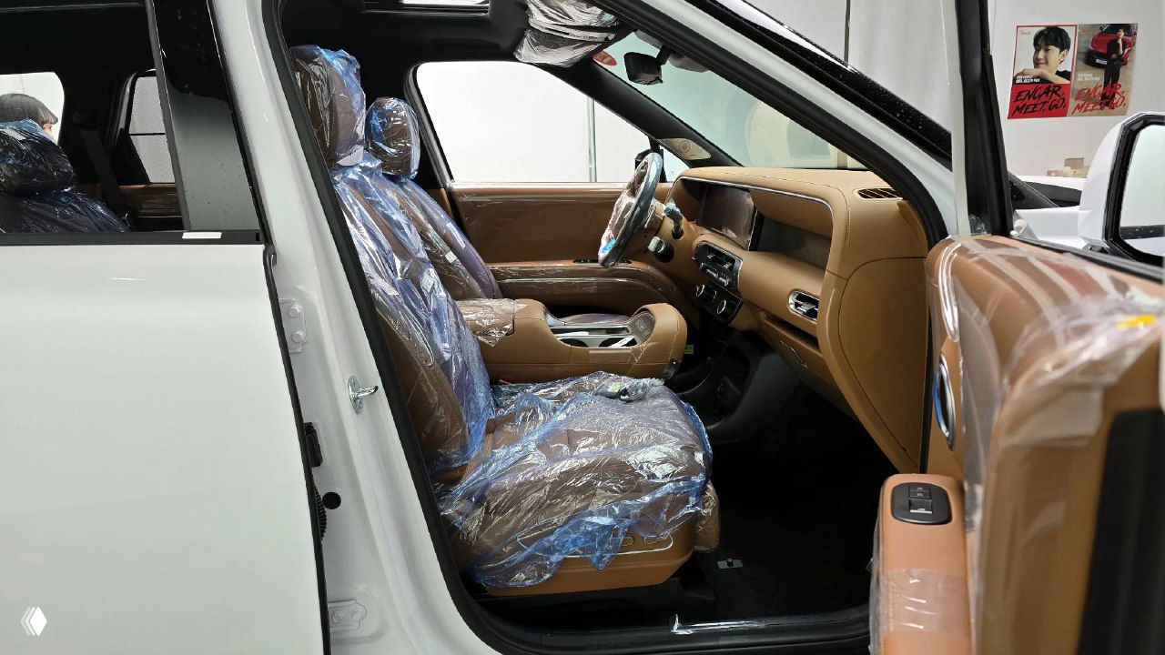 Открытая передняя дверь и вид на передние сиденья Hyundai Palisade, сиденья в защитной плёнке, видна внутренняя отделка двери.