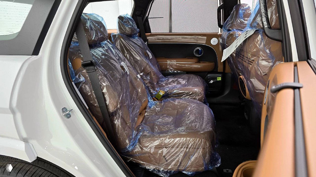 Задний ряд сидений Hyundai Palisade с коричневой кожаной обивкой, сиденья покрыты защитной плёнкой, вид с открытой задней двери.