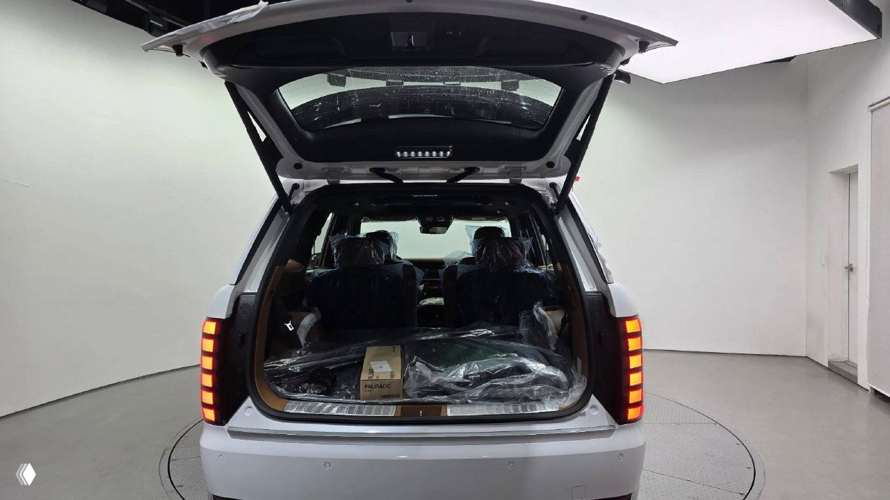 Открытый багажник Hyundai Palisade 2026 на поворотной платформе шоу-рума, видна грузовая зона и упакованные аксессуары внутри.