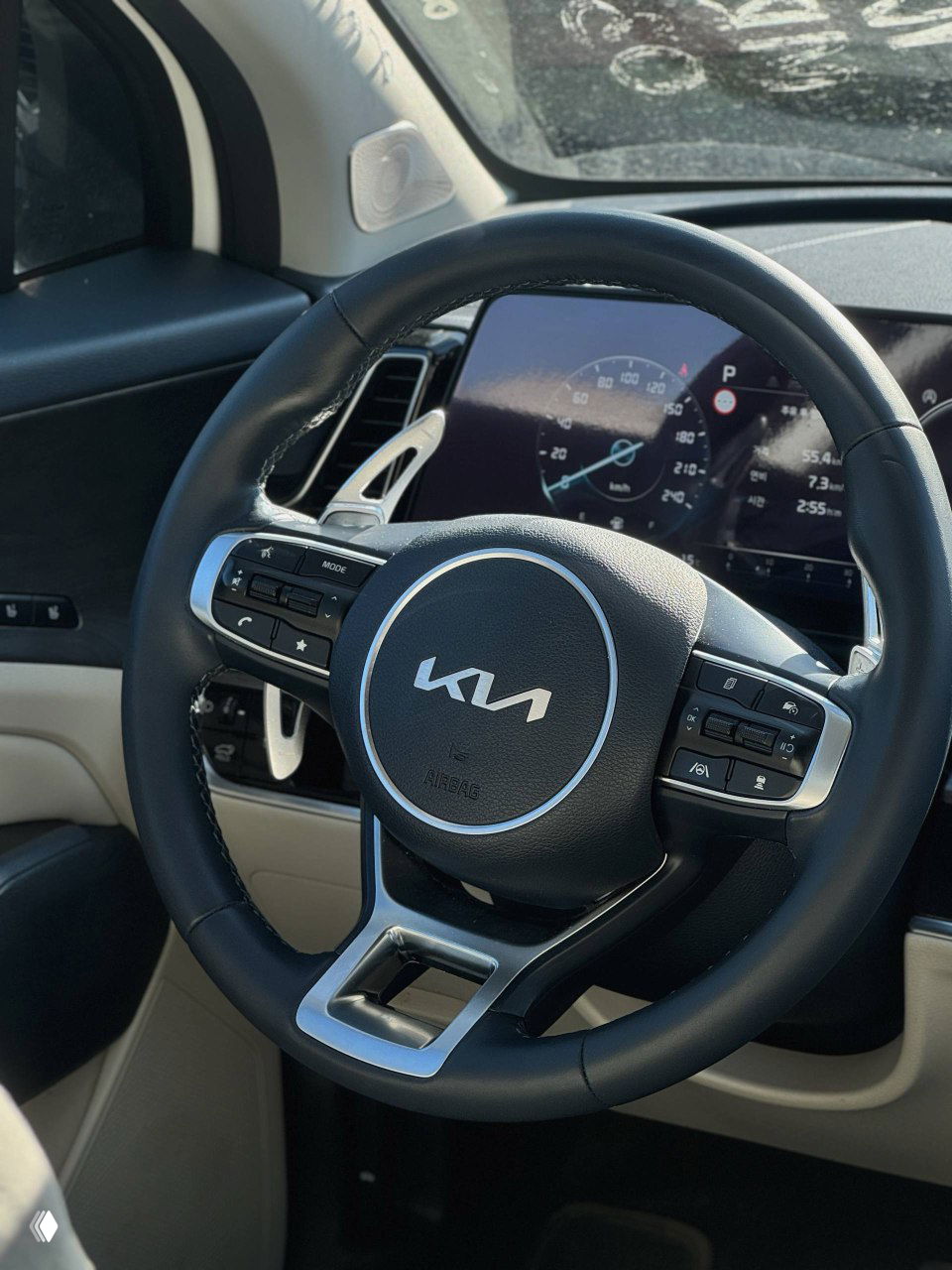 Крупный план руля KIA с логотипом, элементы управления на руле и цифровая приборная панель в салоне автомобиля, освещение дневное.