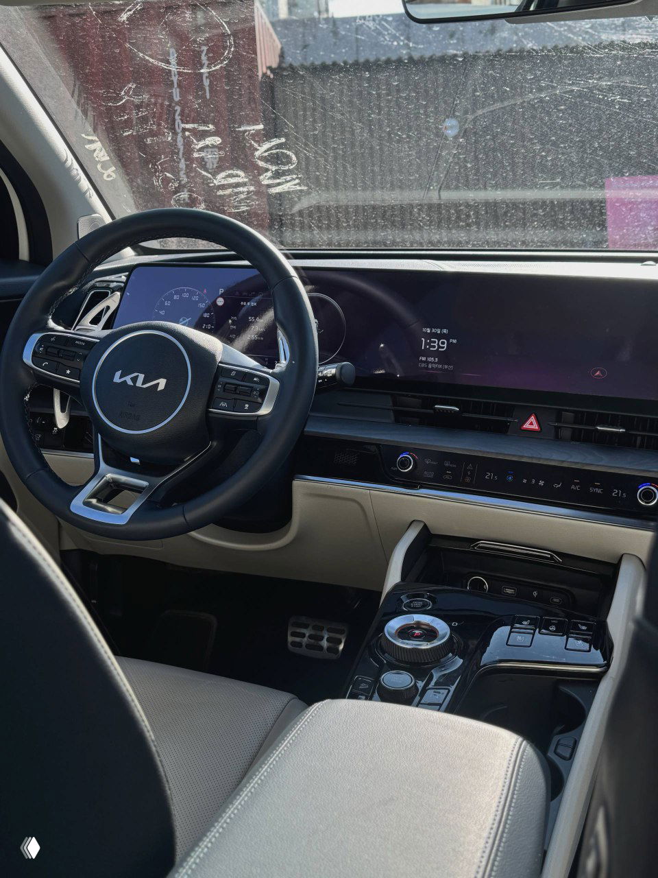 Широкий план центральной части салона KIA Sportage: мультимедийный экран, приборная панель и руль, вид с переднего пассажирского места.