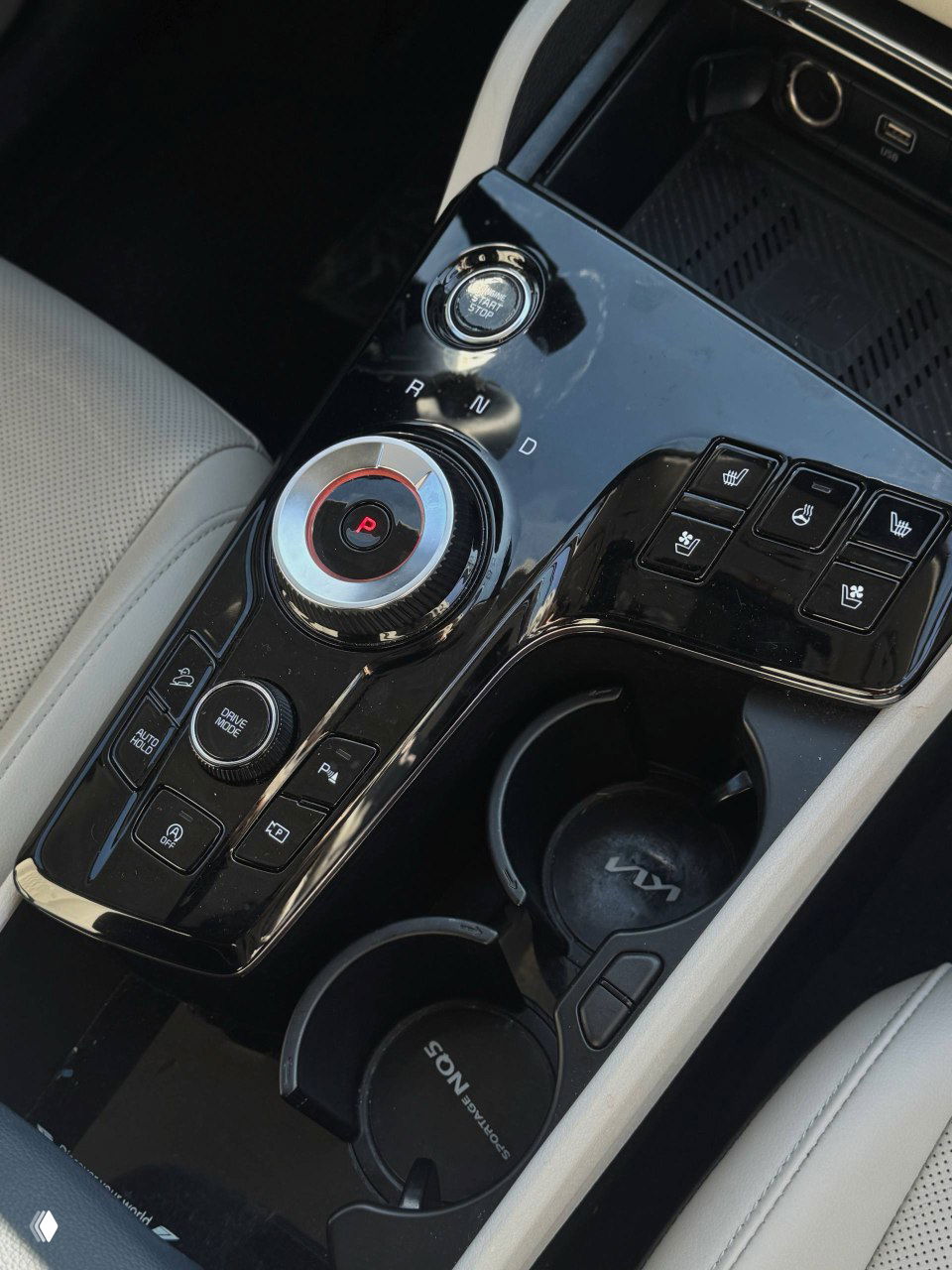 Ближний вид на консоль между сиденьями: селектор передач, кнопки управления климатом и подстаканники в салоне KIA Sportage.