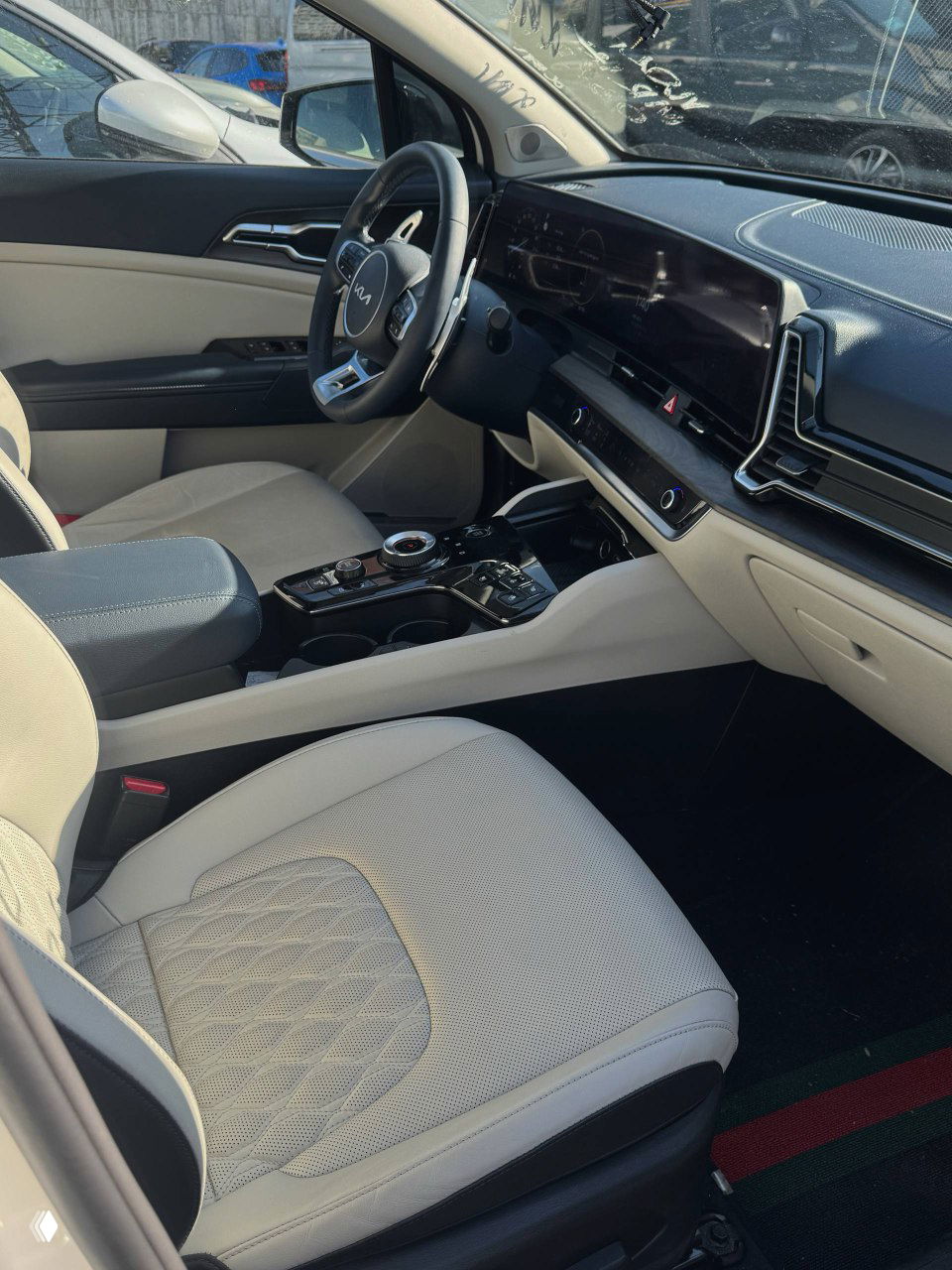 Вид на передние сиденья и центральный туннель KIA Sportage: кожаная отделка светлого цвета, элементы управления и подлокотник.