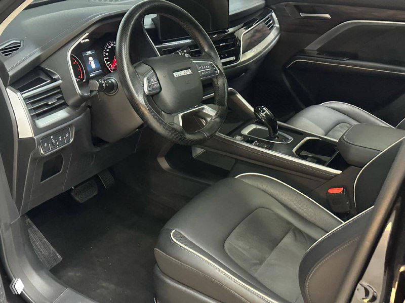 Передняя часть салона Haval H6: водительское сиденье, руль, центральная консоль и элементы отделки комбинированной кожи и вставок.