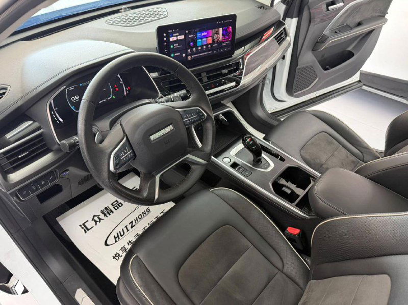 Вид на салон водителя Haval H6 с открытой дверью: руль, рычаг переключения, сиденья и отделка передней части интерьера