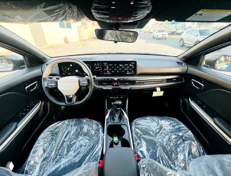 Салон KIA K4: центральная консоль с мультимедийным экраном и приборной панелью, передние сиденья защищены пленкой, современный интерьер.