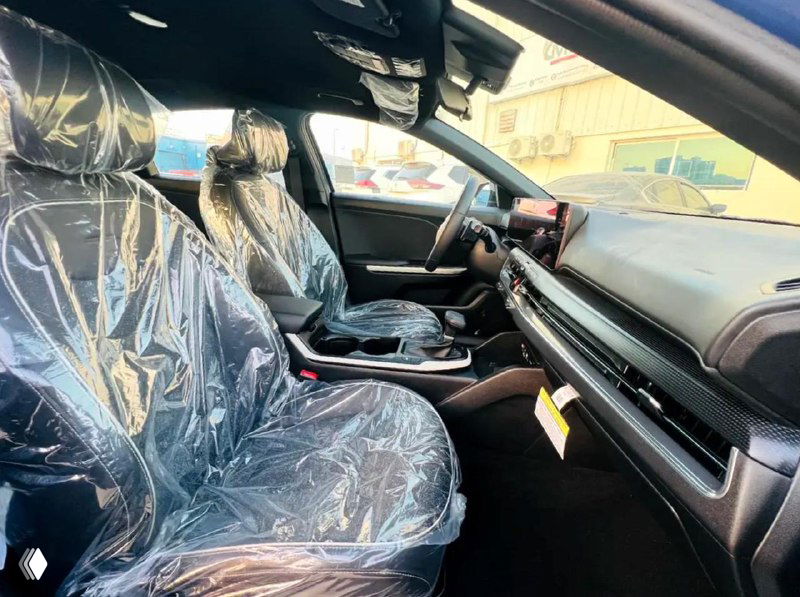 Интерьер KIA K4, вид с пассажирской стороны: торпедо, элементы управления и передние сиденья в защитной пленке, чистый салон без персон.