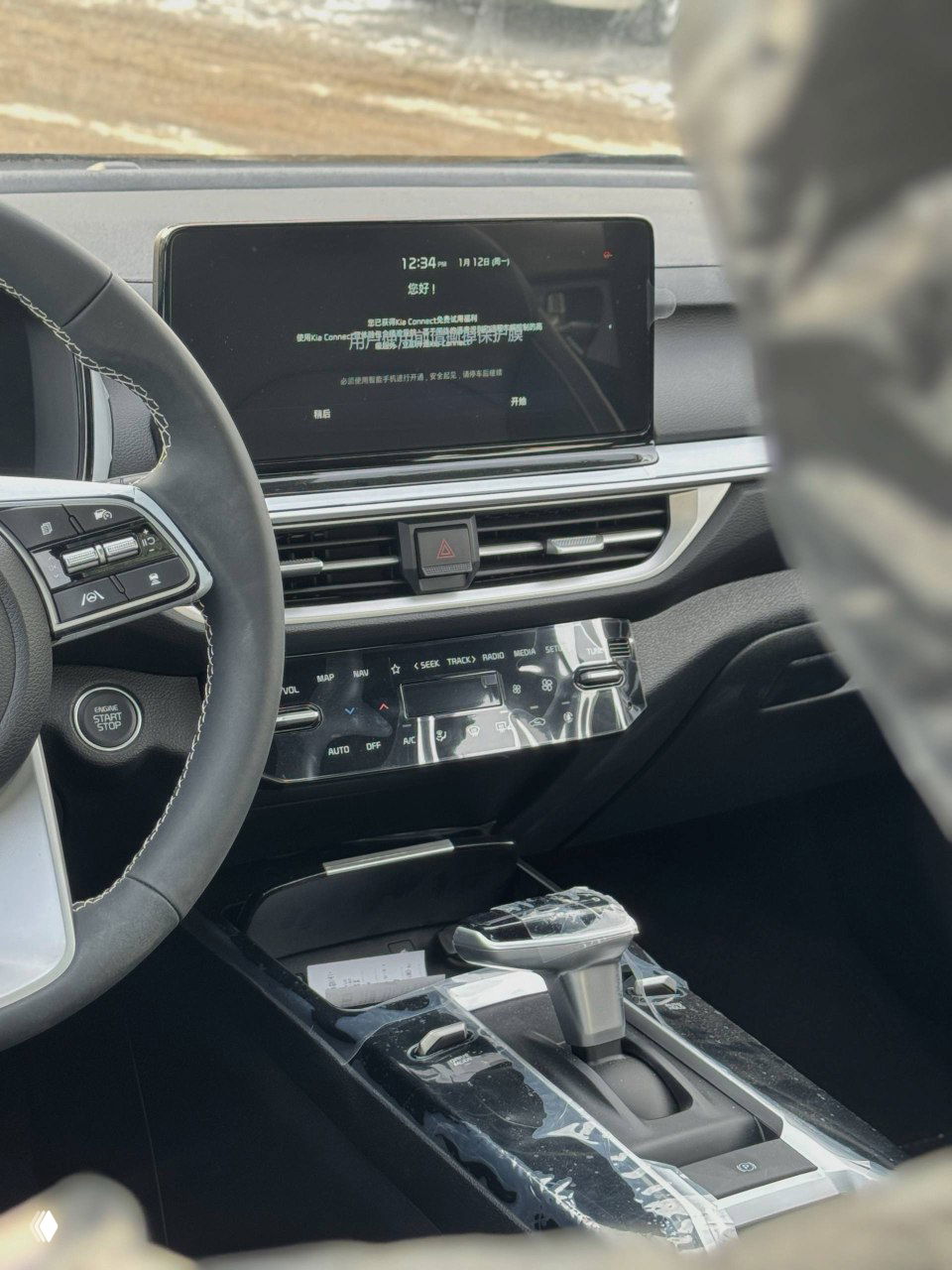 Центральная консоль и мультимедийный дисплей KIA K3, вид на селектор коробки передач и сенсорную панель управления климатом.