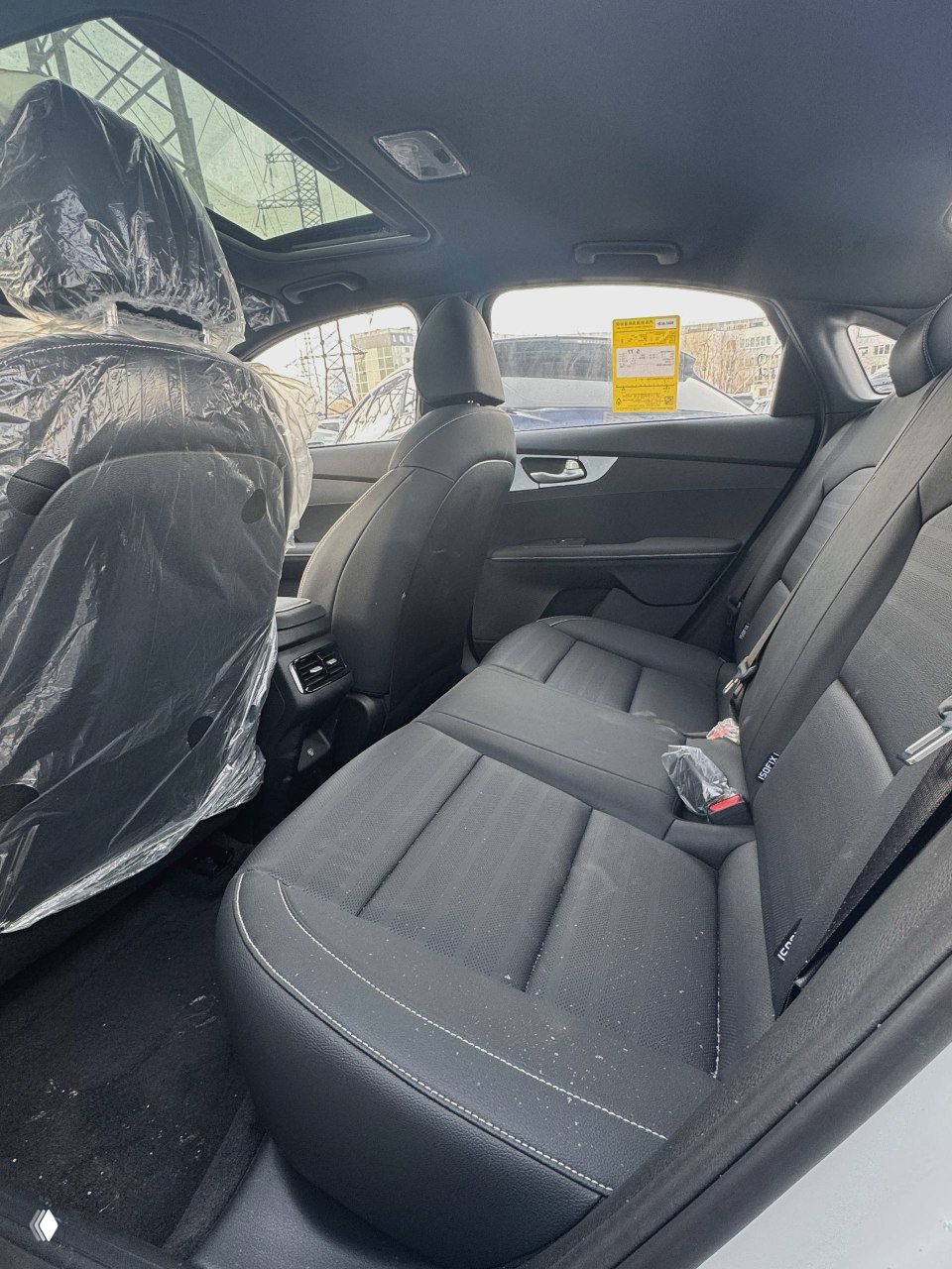 Задний ряд сидений KIA K3 с чёрной тканевой обивкой, вид на простор салона и заднюю часть кабины с упакованными элементами.