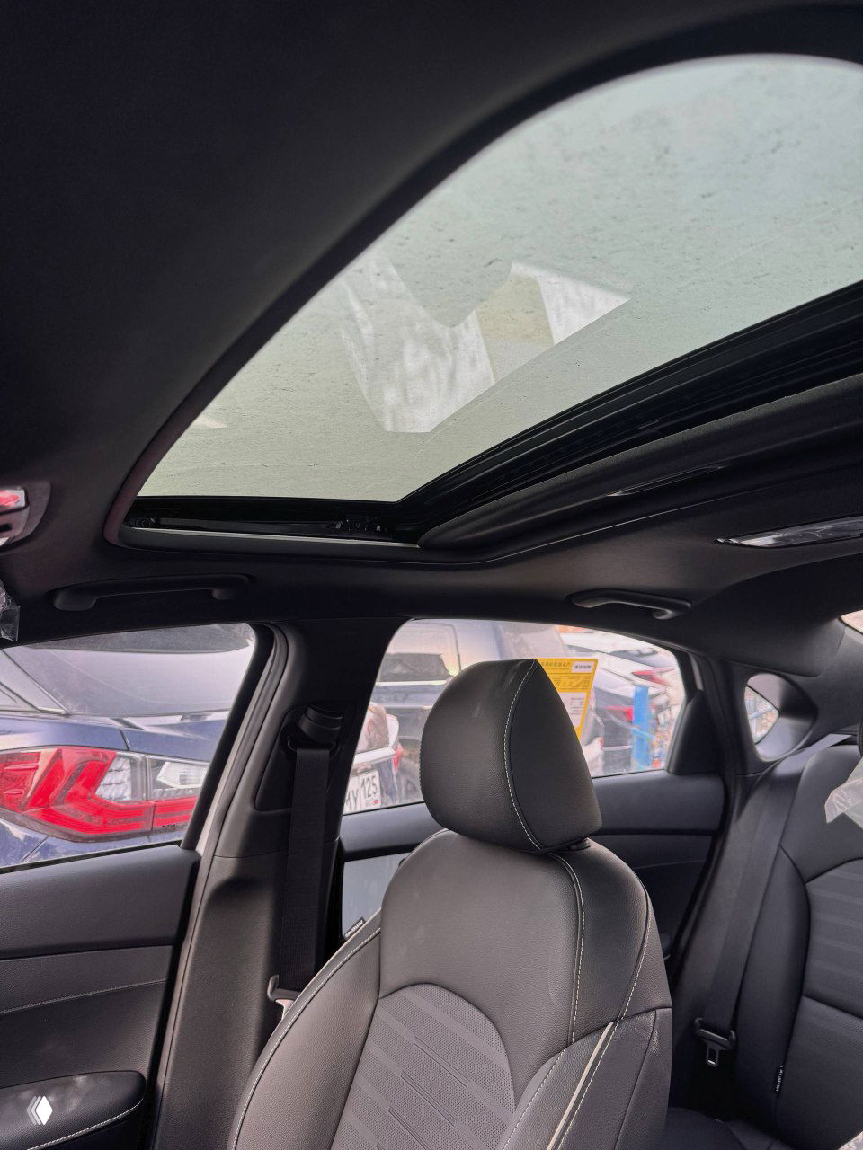 Панорамный люк в крыше KIA K3, вид из салона наружу на соседние автомобили и небо, части сидений защищены плёнкой.