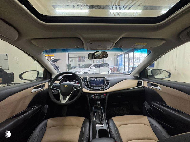 Вид салона Chevrolet Cruze через лобовое стекло: панорамная крыша, передние сиденья и центральная консоль в светлом оформлении интерьера.