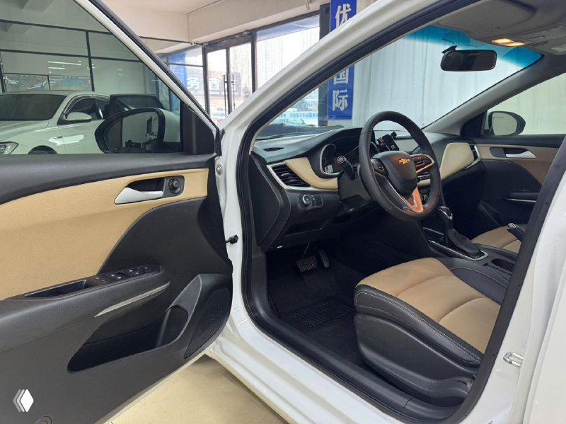 Открытая передняя дверь Chevrolet Cruze, вид на водительское место и отделку дверной панели в бежево‑черной гамме; сиденье и руль видны в профиль.