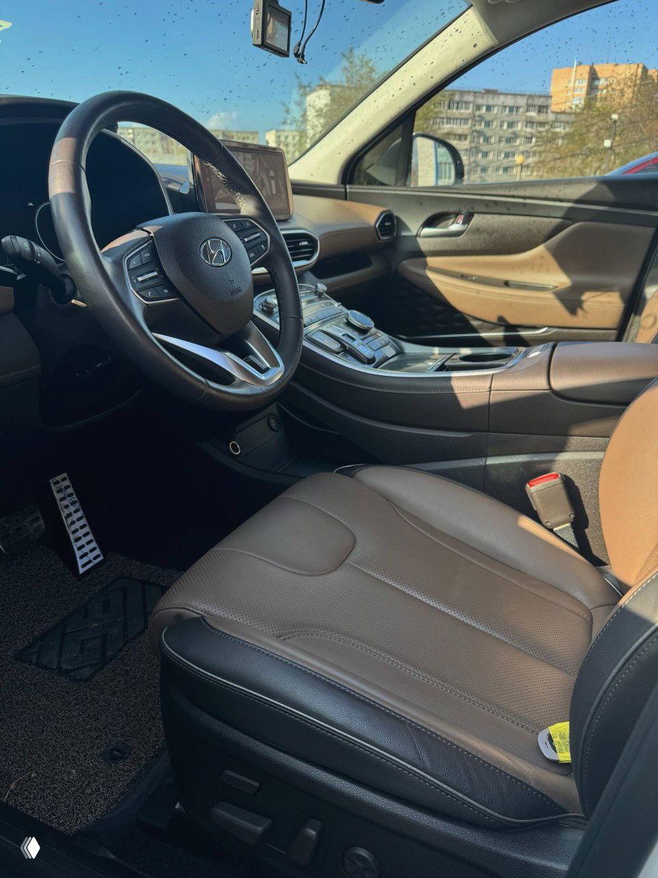 Переднее пассажирское и водительское сиденья коричневой кожи; общий вид салона и центральной консоли со стороны дверного проёма.