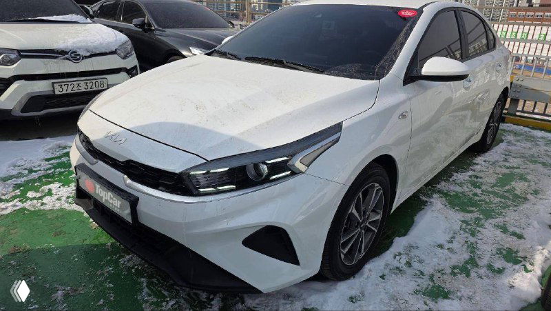 Белый KIA K3 на открытой стоянке с налётом снега, вид спереди с акцентом на фары и капот, фотография для проверки кузова.