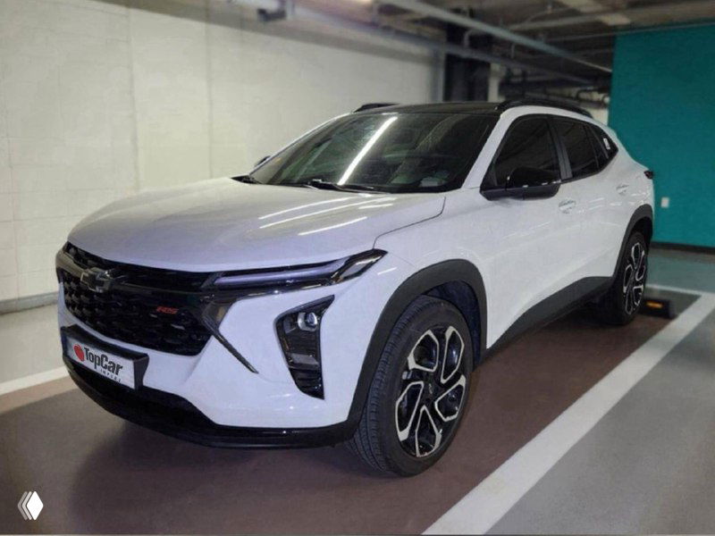Белый Chevrolet Trax RS на крытой парковке, профиль автомобиля и колёса видны, снимок демонстрирует общий внешний вид для экспорта.
